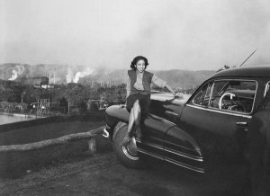 Charles "Teenie" Harris - Doris Clark (Moody) seated on Buick car with steel mill in background, Clairton, ca. 1945