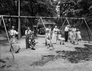 Charles "Teenie" Harris - Men standing behind elderly women seated on swings, at Highland Park picnic, August 1952