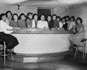 Charles "Teenie" Harris - Group portrait of fourteen young women from Kolesque Club, posed behind light colored upholstered bar, ca. 1950