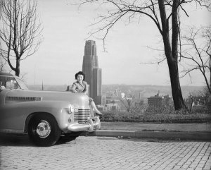 Charles "Teenie" Harris - Clara Itsue Funasaki seated on Cadillac, with University of Pittsburgh and Cathedral of Learning in background, Oakland, 1946